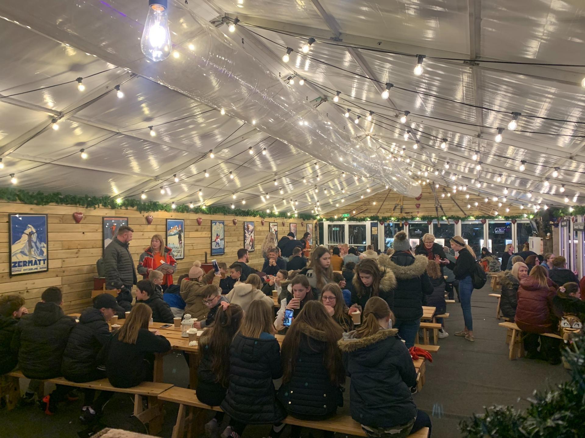 A busy festoon-lit marquee with wooden walls and picnic tables at Park Farm, Bodiam
