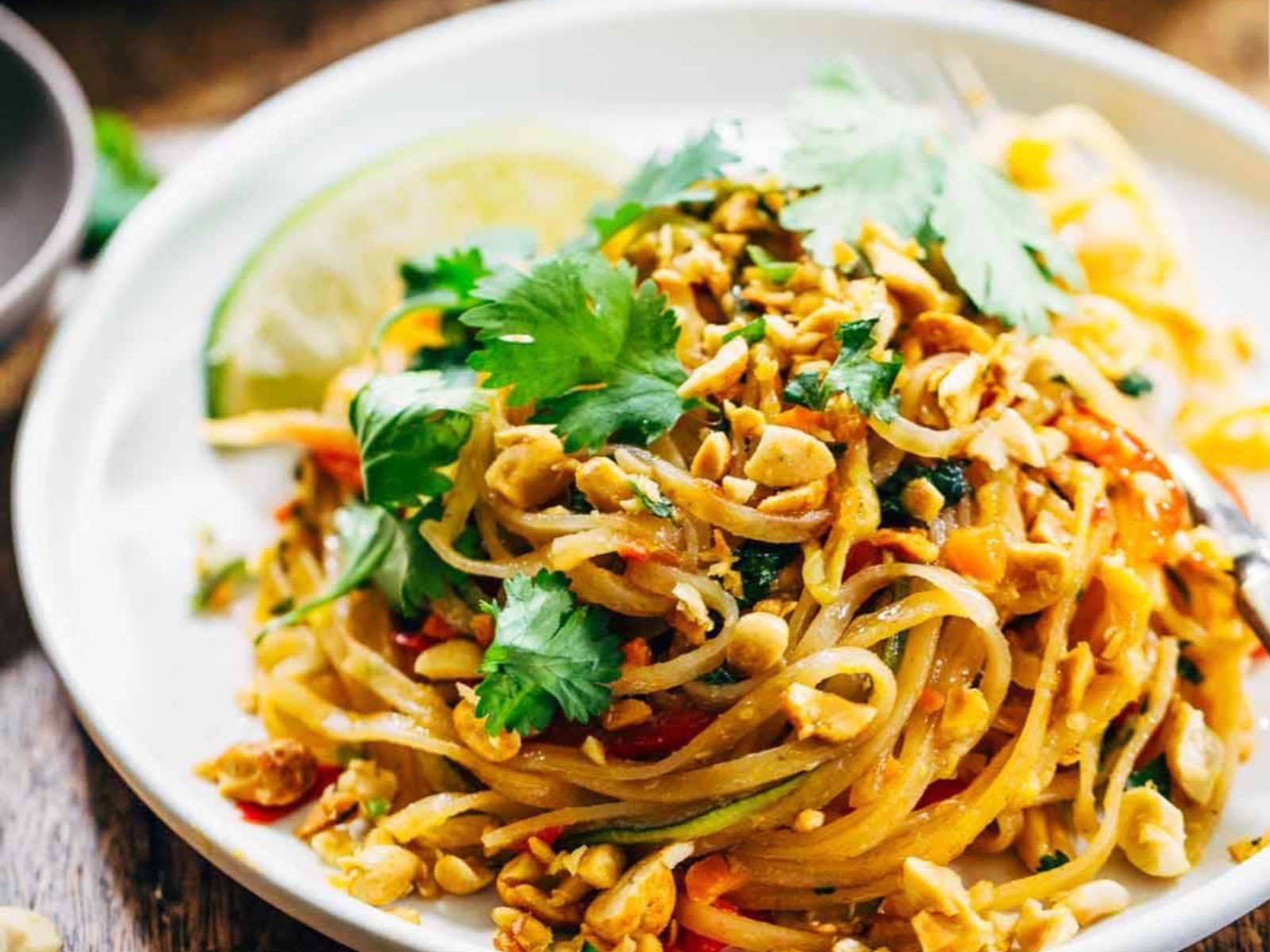 A plate of pad thai with peanuts, coriander and lime
